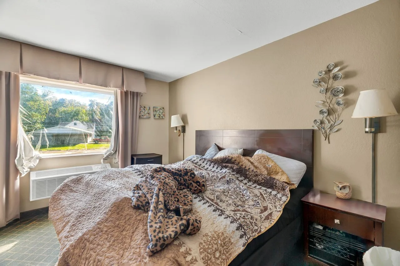 A room with a king bed, a nightstand, a reading lamp and a large window