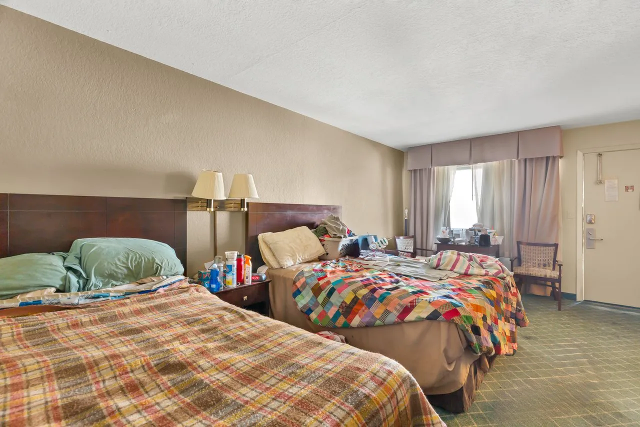 A room with two beds, wall lamps between them and a window with curtains